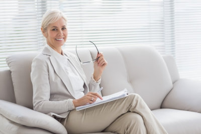 mental health professional holding eyeglasses sitting on sofa smiling